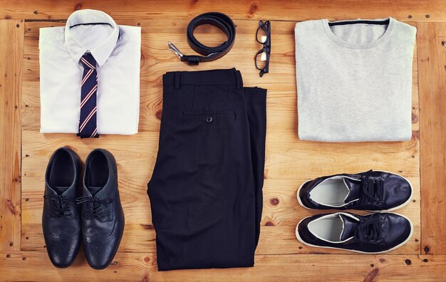 Men’s clothing and accessories neatly arranged on a wooden surface, including shirts, pants, shoes, belt, tie, and glasses.
