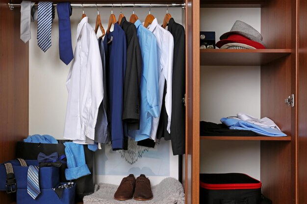 Neatly organized wardrobe with shirts, ties, jackets, shoes, folded clothes, and hats arranged on hangers, shelves, and storage boxes.