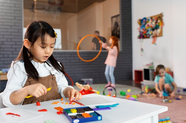 Children playing and working with toys and crafts in a bright classroom.
